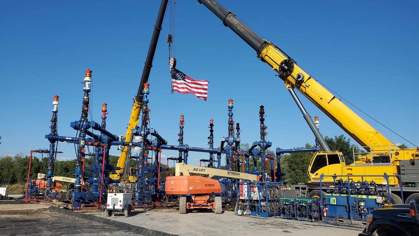 Completion wellheads and cranes with U.S. flag on a multi-well pad